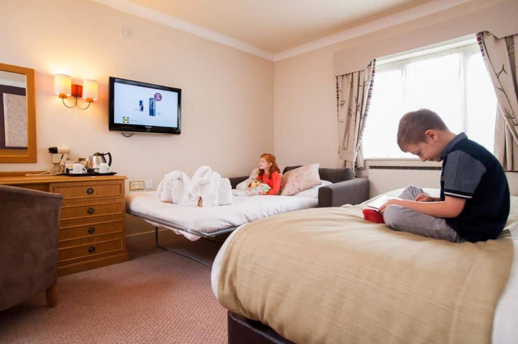 Kids watching TV, playing games and relaxing in family room with comfortable sofa bed at family-friendly hotel, Abbey Hotel Golf & Spa