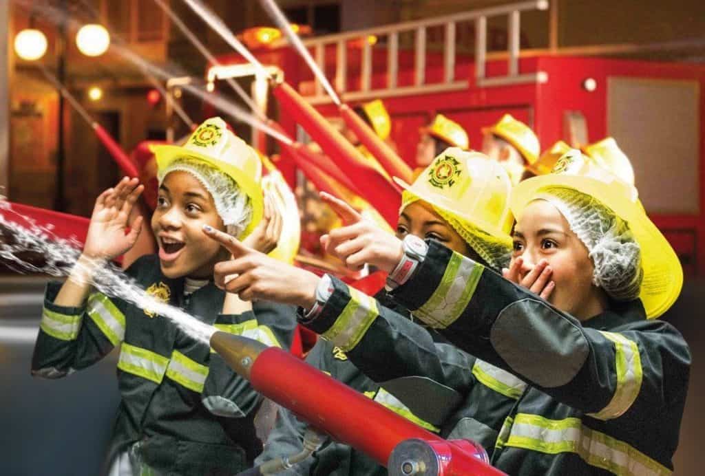 kids having fun with water hoses and role-playing as firemen and firewomen at kidzania london