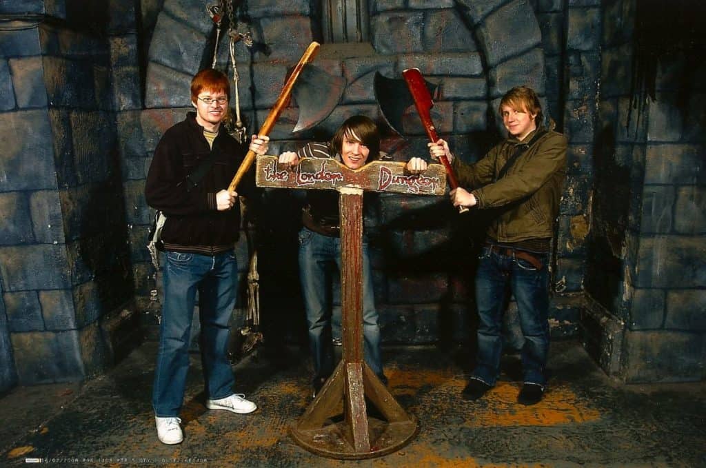 teenagers posing on the scary  guillotine as they learn about london's dark and gruesome history at the london dungeon